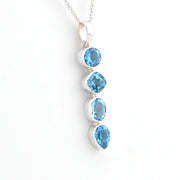 A silver pendant necklace featuring four vertically aligned round-cut light blue gemstones in a silver bezel setting, suspended from a silver chain against a plain white background.