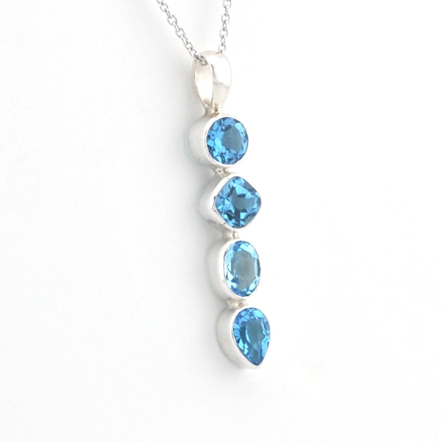 A silver pendant necklace featuring four vertically aligned round-cut light blue gemstones in a silver bezel setting, suspended from a silver chain against a plain white background.