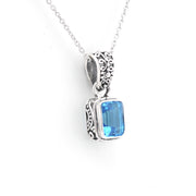 A sterling silver pendant necklace featuring a rectangular blue gemstone in an ornate, textured bezel setting, suspended from a delicate silver chain against a plain white background.