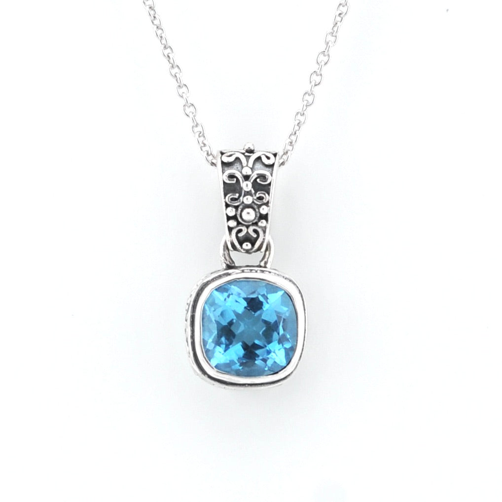 A silver pendant necklace featuring a cushion-cut light blue gemstone in a textured silver bezel setting, suspended from a delicate silver chain against a plain white background.