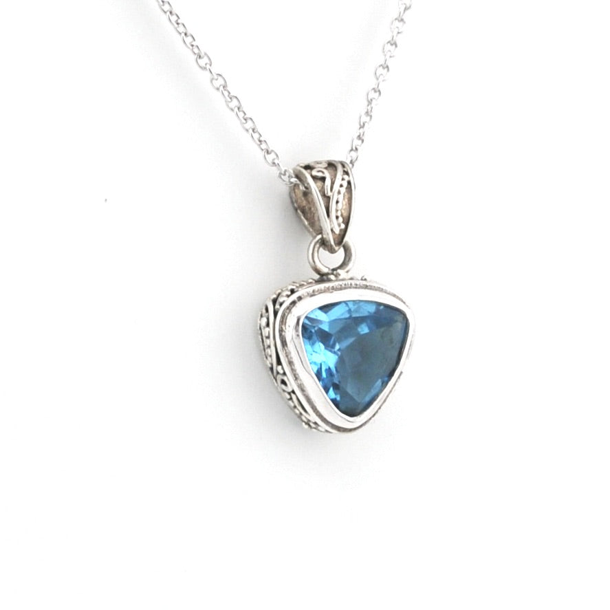 A silver pendant necklace featuring a triangular blue gemstone in an ornate silver bezel setting, suspended from a delicate silver chain against a plain white background.