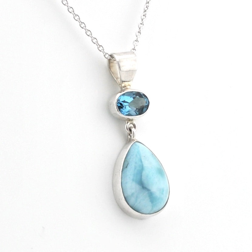 A silver pendant necklace featuring a large teardrop-shaped light blue larimar stone and a smaller oval blue gemstone, displayed on a clean white background.