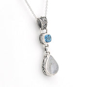A sterling silver pendant necklace featuring a teardrop-shaped light gray moonstone and a smaller square blue gemstone, both set in ornate silver bezels on a delicate silver chain.
