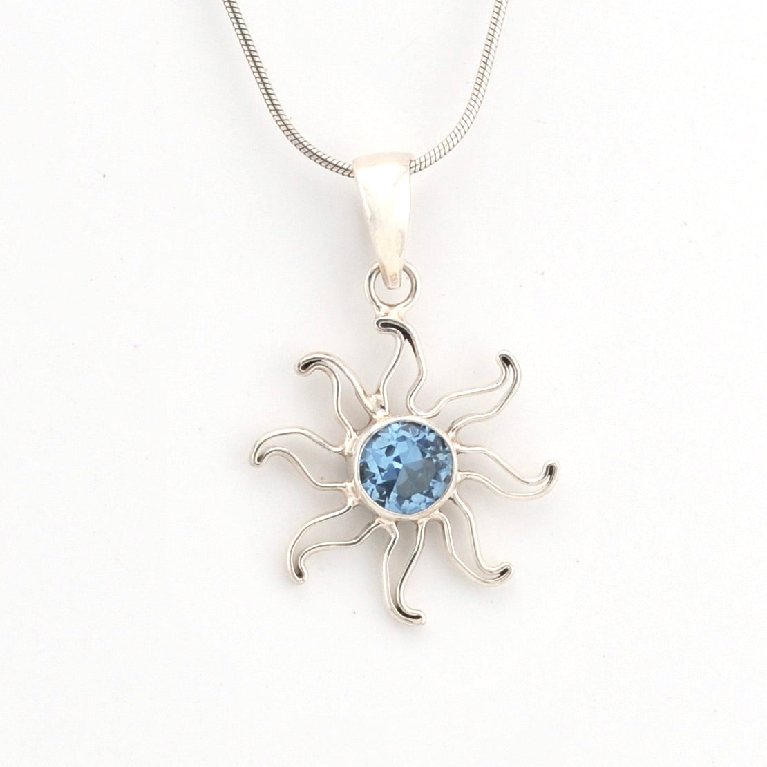 Silver sun-shaped pendant with a blue gemstone on a white background