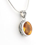 A silver pendant necklace featuring an oval faceted amber-orange gemstone in an ornate silver bezel setting, suspended from a silver snake chain against a plain white background.