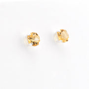 A pair of gold stud earrings with round-cut yellow gemstones in silver prong settings, shown on a plain white background.