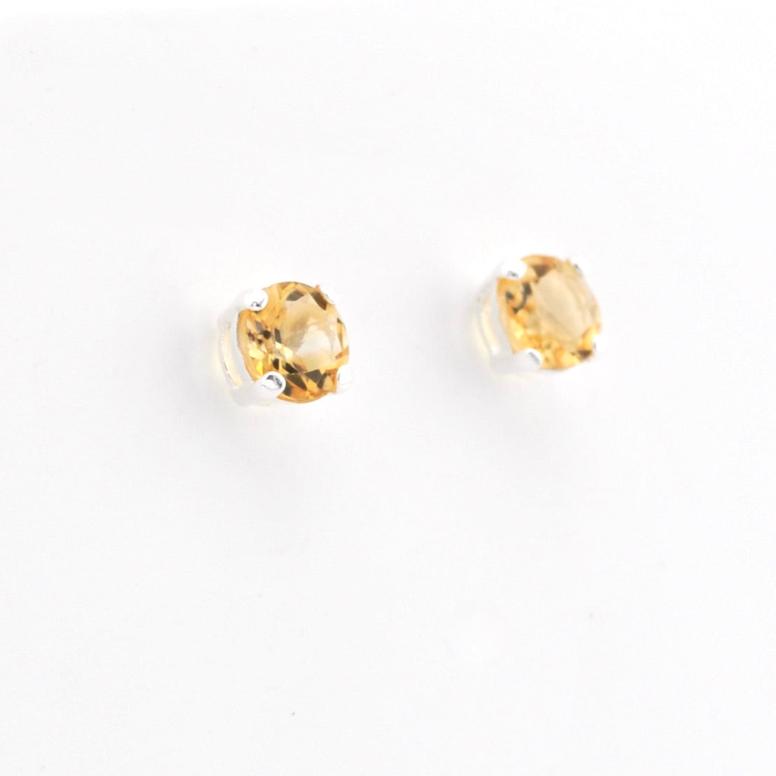A pair of gold stud earrings with round-cut yellow gemstones in silver prong settings, shown on a plain white background.