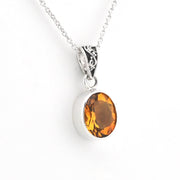 A silver pendant necklace featuring an oval-cut citrine gemstone in a polished bezel setting, suspended from a delicate silver chain against a plain white background.