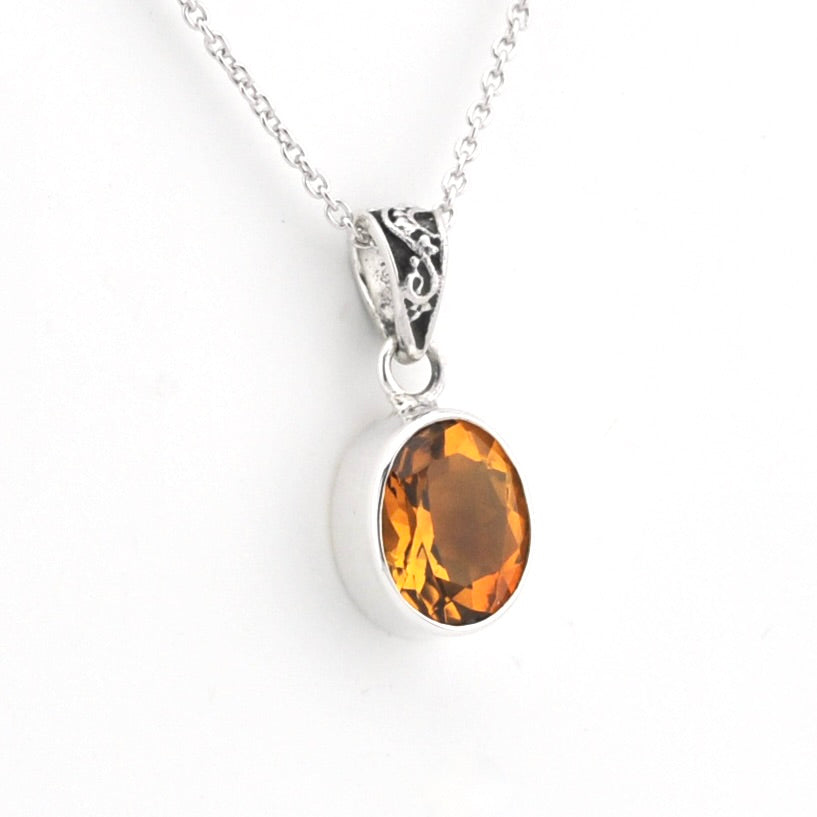 A silver pendant necklace featuring an oval-cut citrine gemstone in a polished bezel setting, suspended from a delicate silver chain against a plain white background.