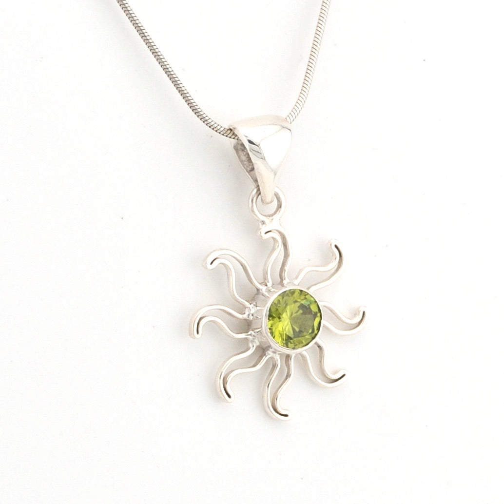 Silver sun-shaped pendant with a green gemstone on a white background