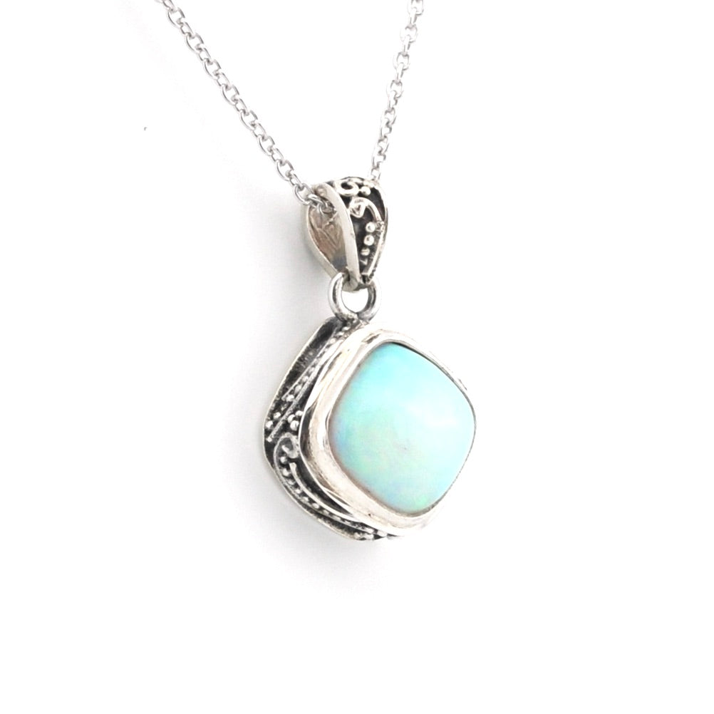 A silver pendant necklace featuring a light blue-green iridescent stone in an ornate silver bezel setting, suspended from a delicate silver chain against a plain white background.