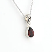 A silver teardrop pendant necklace featuring a faceted dark red gemstone, suspended from a delicate silver chain against a plain white background.