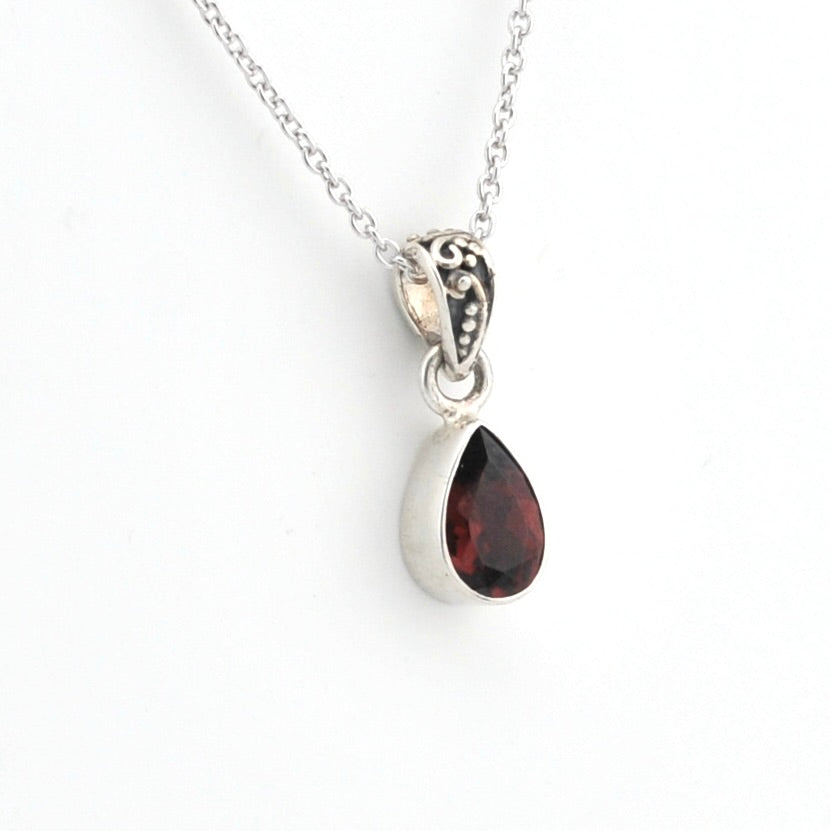 A silver teardrop pendant necklace featuring a faceted dark red gemstone, suspended from a delicate silver chain against a plain white background.