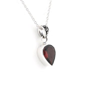 A silver pear shaped pendant necklace featuring a dark red gemstone, suspended from a delicate silver chain on a white background.