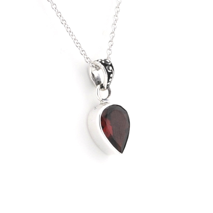 A silver pear shaped pendant necklace featuring a dark red gemstone, suspended from a delicate silver chain on a white background.