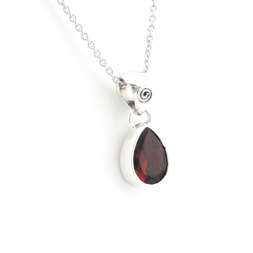 A silver teardrop pendant necklace featuring a faceted dark red gemstone, suspended from a delicate silver chain on a plain white background.