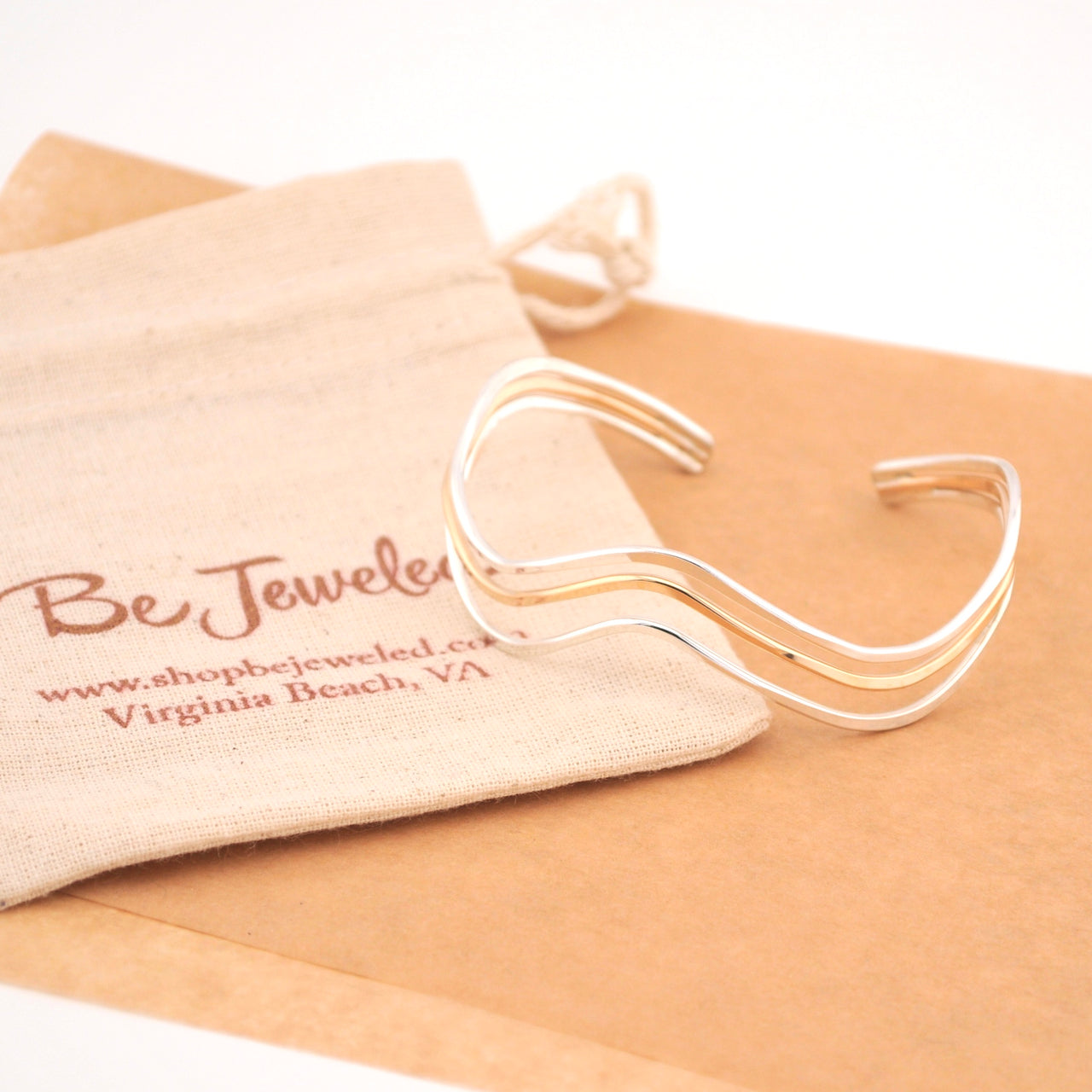 Gold and silver bracelet on a beige surface with a branded pouch.