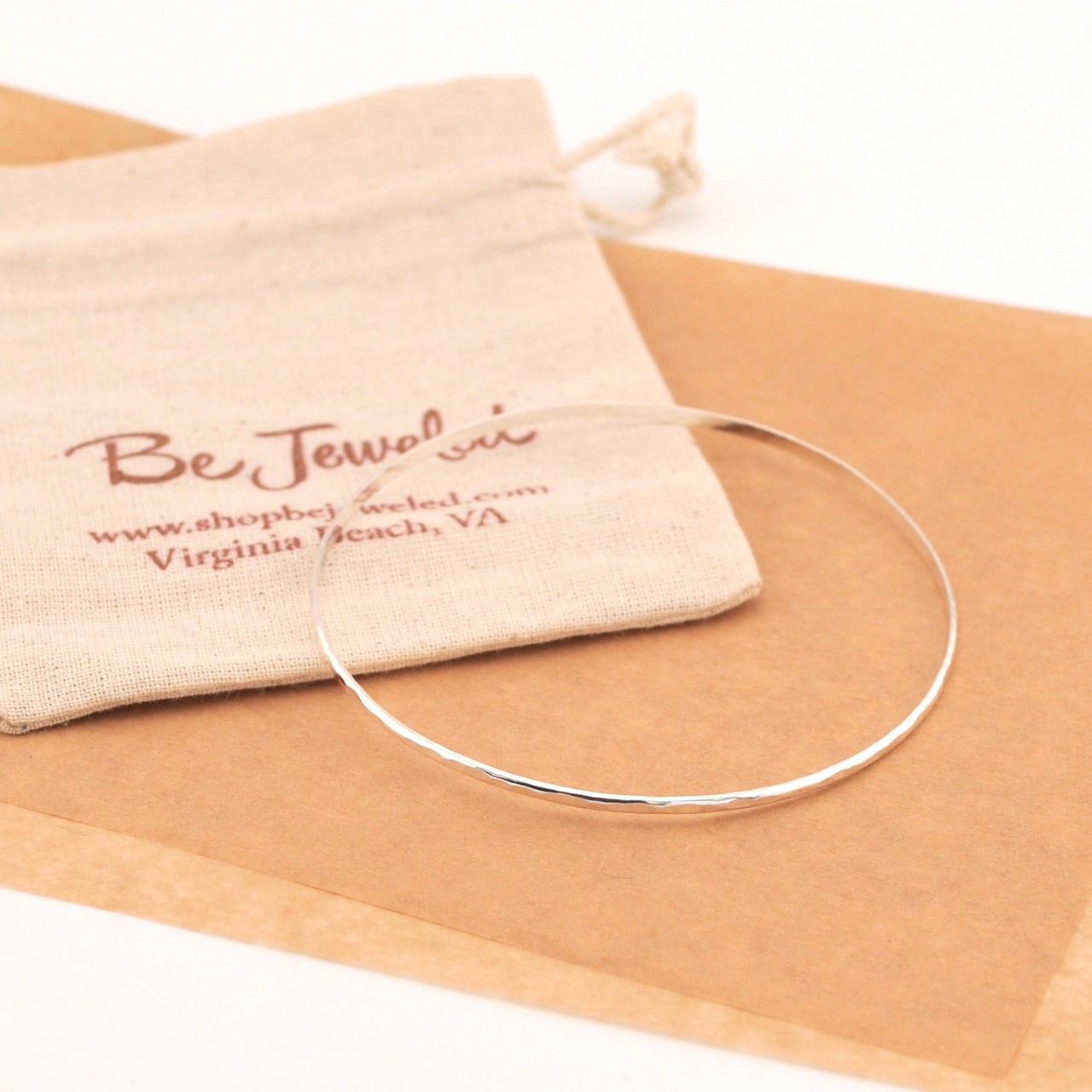 Silver necklace on brown paper with a branded pouch