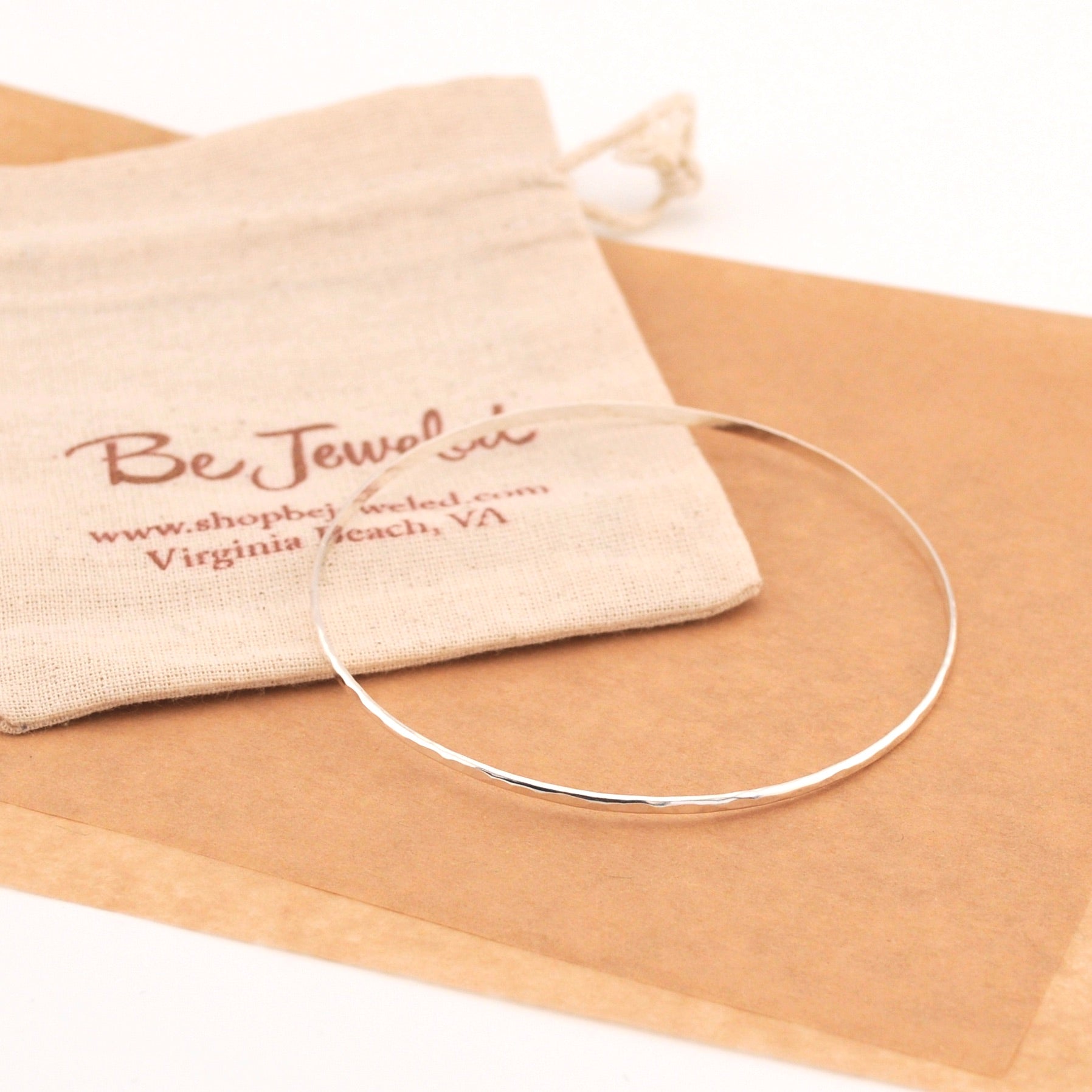 Silver necklace on brown paper with a branded pouch