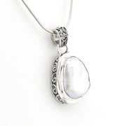 A sterling silver pendant necklace featuring a large, irregular white pearl set in an ornate filigree bezel, suspended from a matching silver snake chain against a plain white background.