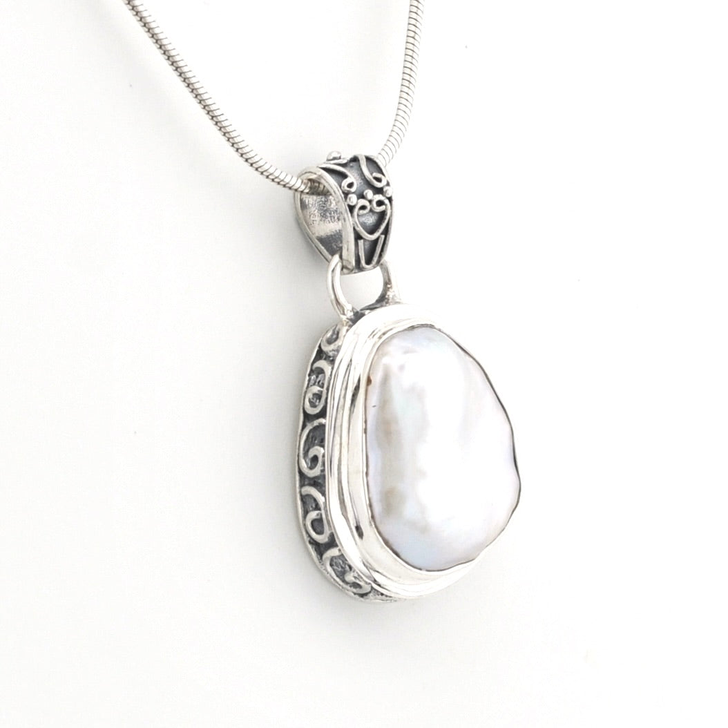 A sterling silver pendant necklace featuring a large, irregular white pearl set in an ornate filigree bezel, suspended from a matching silver snake chain against a plain white background.