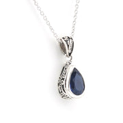 A silver teardrop pendant necklace featuring a deep blue gemstone, displayed on a clean white background.