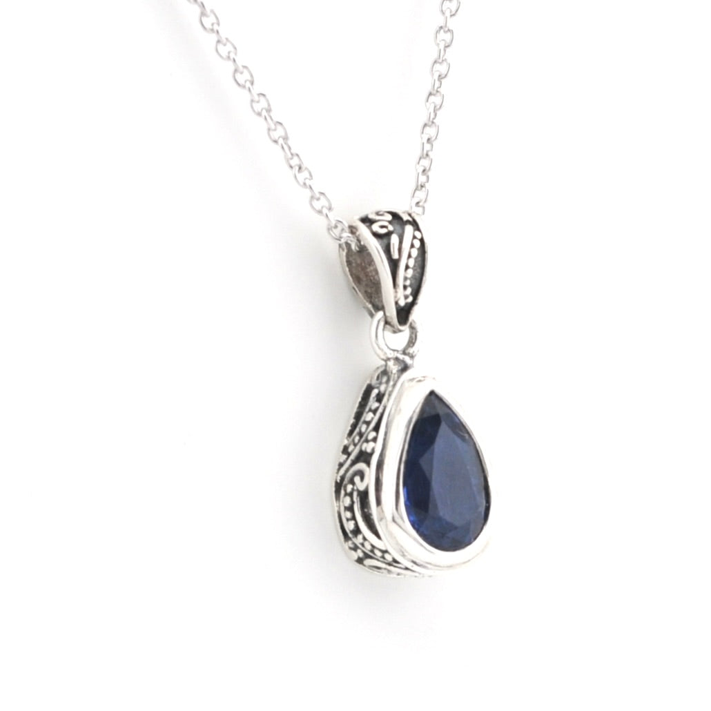 A silver teardrop pendant necklace featuring a deep blue gemstone, displayed on a clean white background.