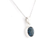 A silver pendant necklace featuring an oval-cut dark blue faceted gemstone in a polished silver bezel setting, suspended from a delicate silver chain against a plain white background.