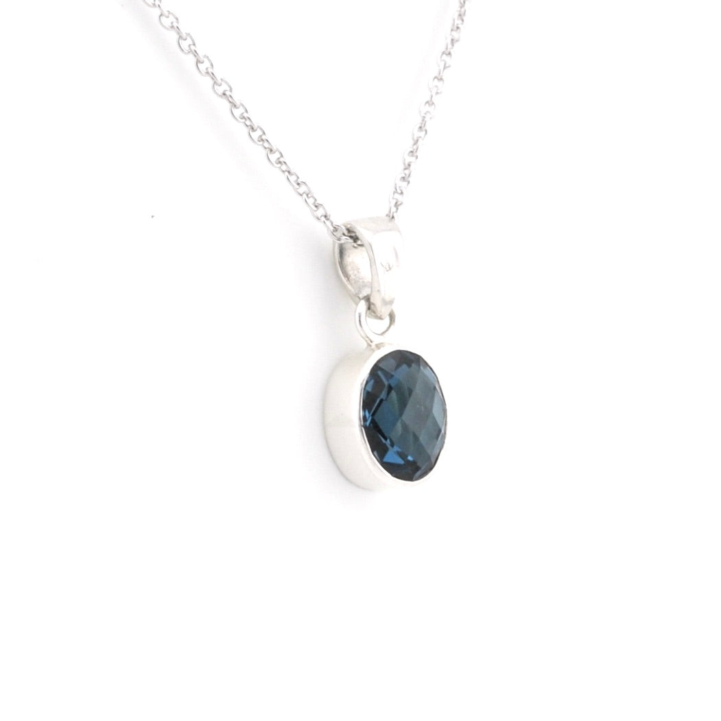 A silver pendant necklace featuring an oval-cut dark blue faceted gemstone in a polished silver bezel setting, suspended from a delicate silver chain against a plain white background.