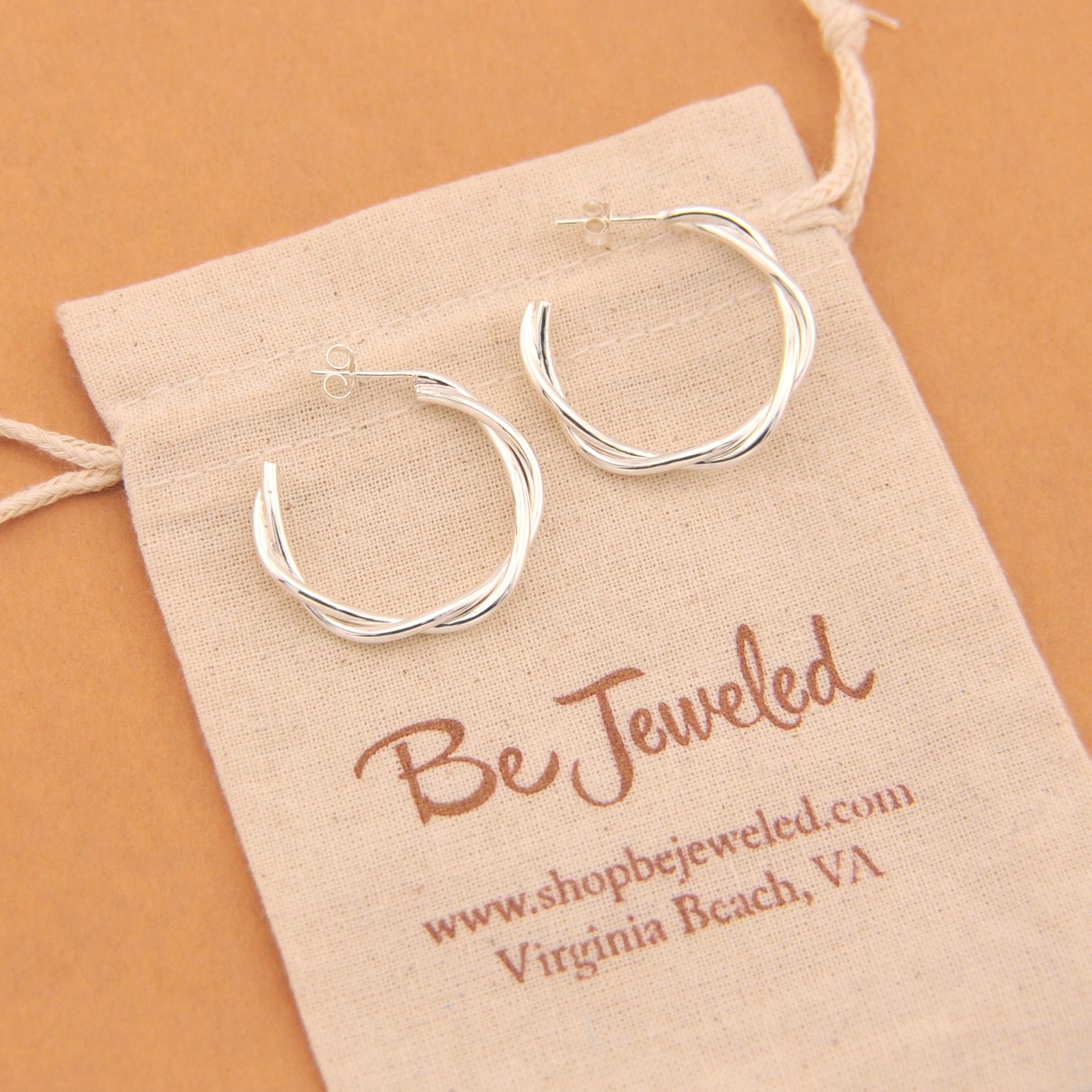 Silver hoop earrings on a 'Be Jeweled' branded pouch with a beige background