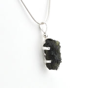A silver snake chain necklace with a raw, rough dark green stone pendant held in a silver bezel setting, shown against a plain white background.