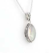 A silver pendant necklace featuring an oval iridescent moonstone gemstone in an ornate, filigree-set silver frame, suspended from a delicate silver chain against a plain white background.