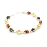 A silver link bracelet featuring oval-cut natural Baltic amber beads in various colors including yellow, orange, and dark brown, displayed on a clean white background.