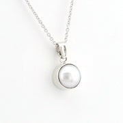 A silver pendant necklace featuring a polished silver bezel holding a round white pearl, suspended from a delicate silver chain against a plain white background.