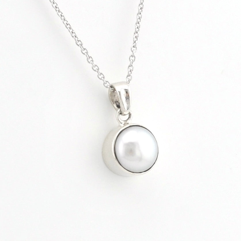 A silver pendant necklace featuring a polished silver bezel holding a round white pearl, suspended from a delicate silver chain against a plain white background.
