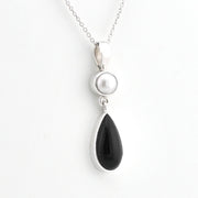 A silver pendant necklace featuring a teardrop-shaped black onyx stone and a round white pearl set in silver on a delicate silver chain, shown against a plain white background.