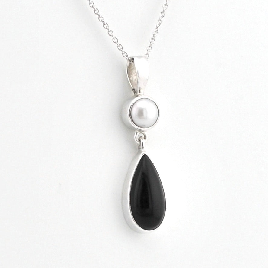 A silver pendant necklace featuring a teardrop-shaped black onyx stone and a round white pearl set in silver on a delicate silver chain, shown against a plain white background.