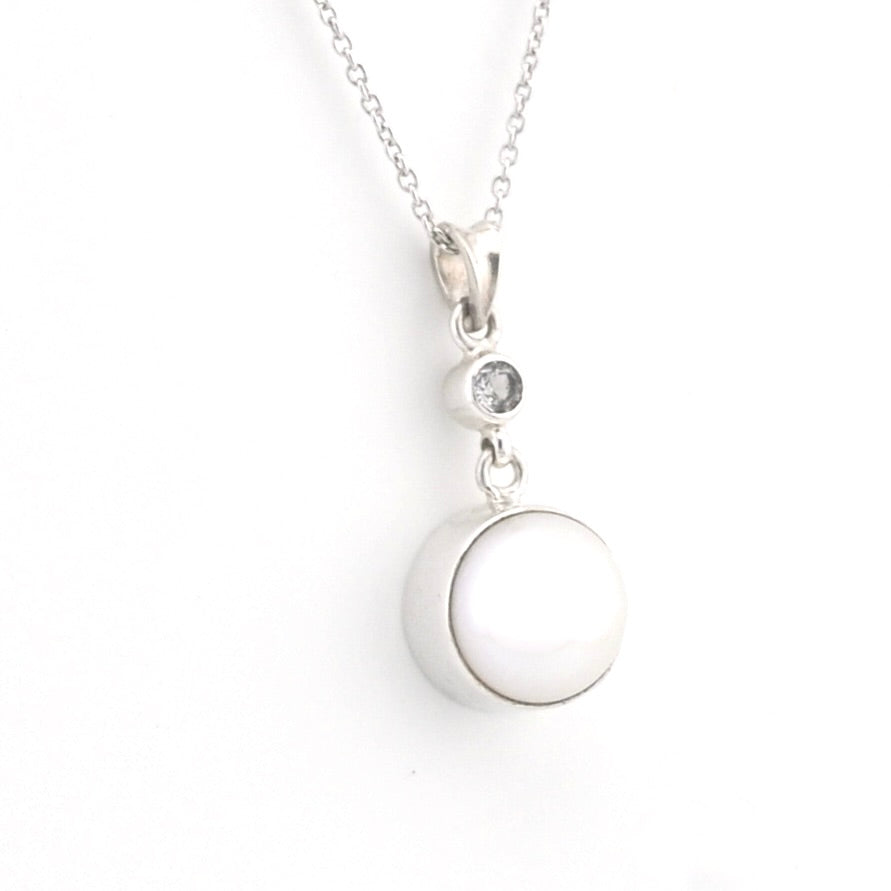 A silver necklace featuring a large, smooth white circular pendant and a smaller clear gemstone accent above it, shown on a plain white background.