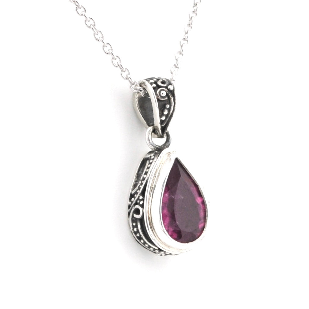 A silver teardrop pendant necklace featuring a faceted dark pink gemstone, set in an ornate silver bezel with a silver chain, shown against a plain white background.