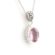 A silver pendant necklace featuring an oval-cut pink gemstone in a textured bezel setting, suspended from a delicate silver chain against a plain white background.
