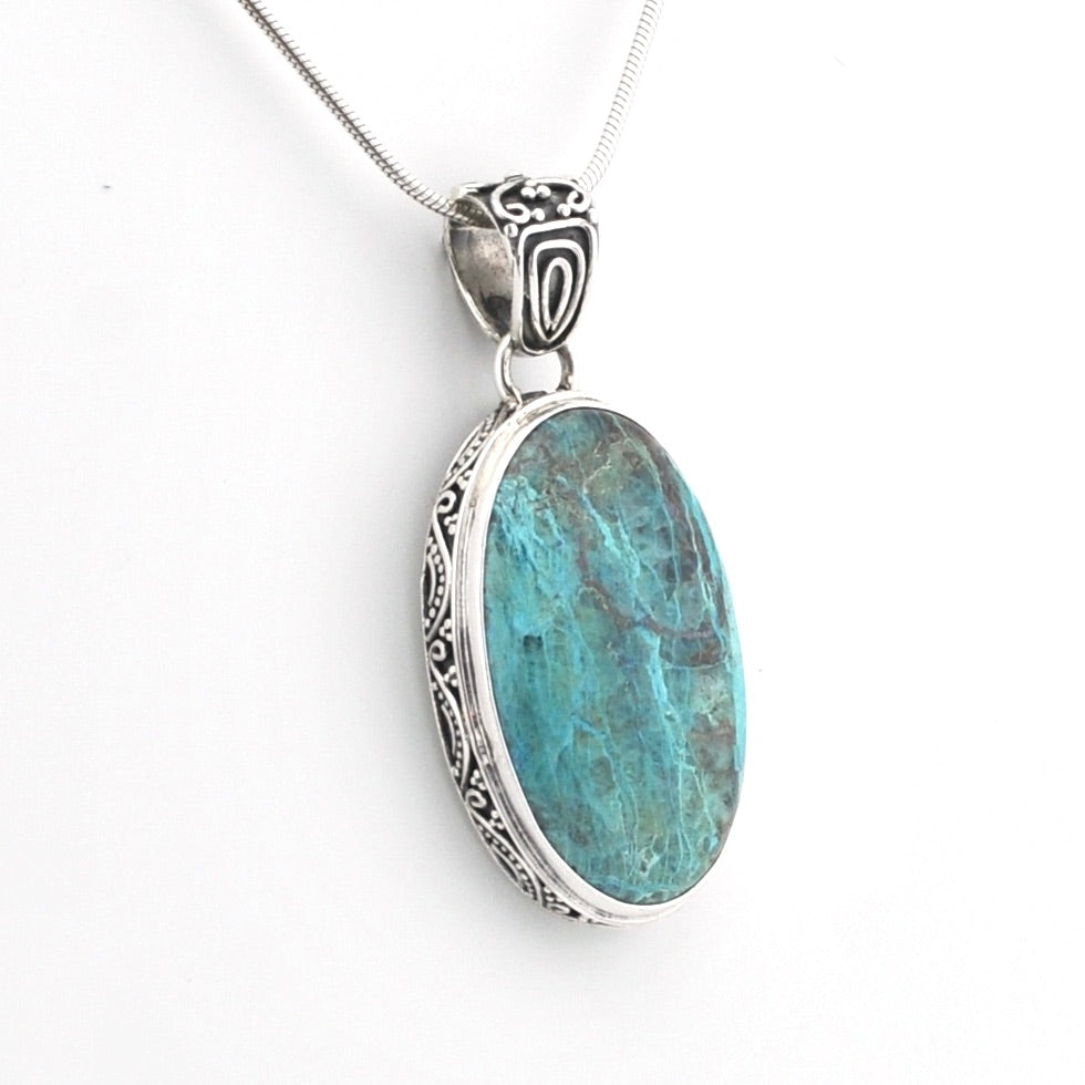 An oval pendant necklace featuring a turquoise-blue marbled stone in a silver bezel with ornate engraved silver borders, suspended from a silver chain on a white background.