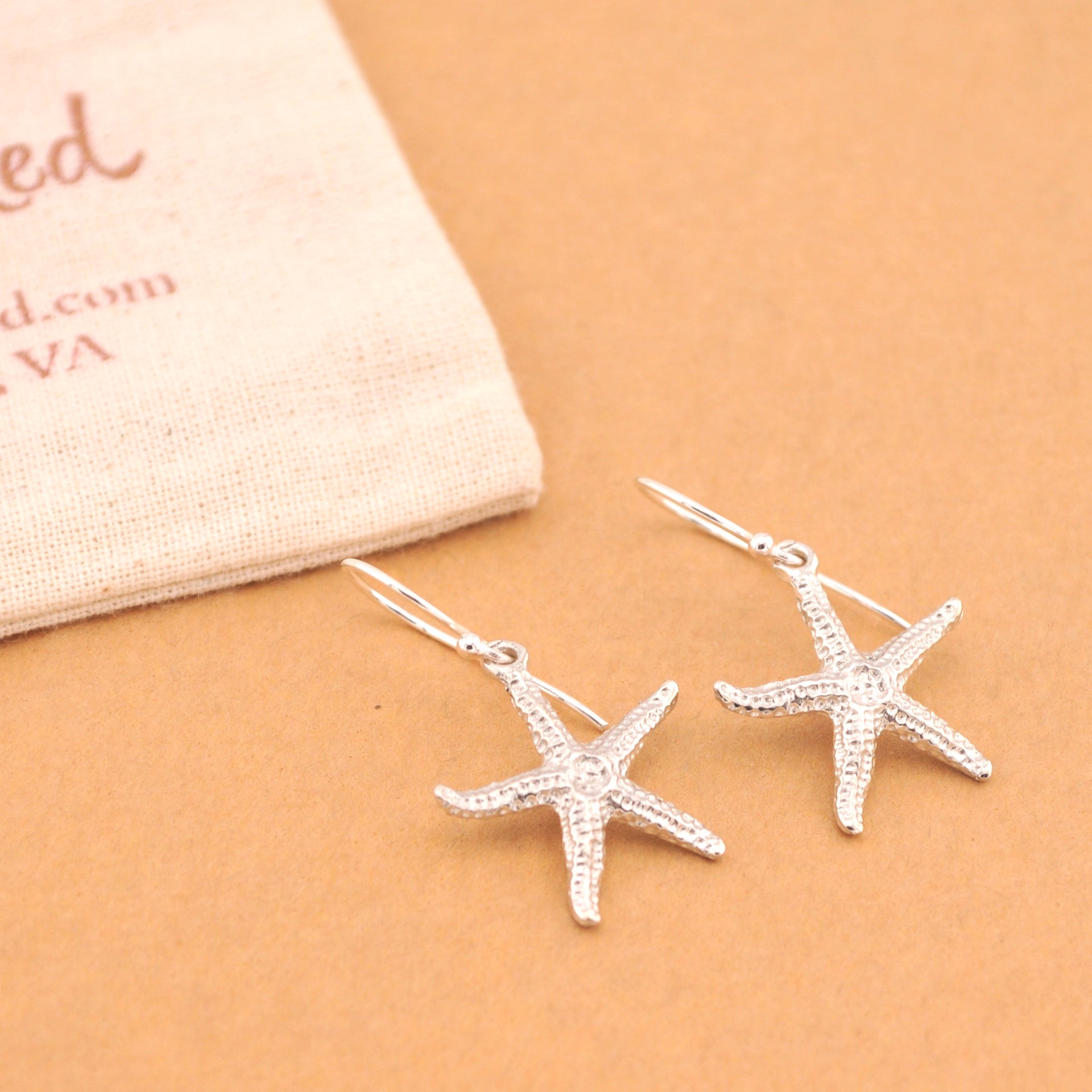 Silver starfish earrings on a beige surface with a jewelry box in the background.