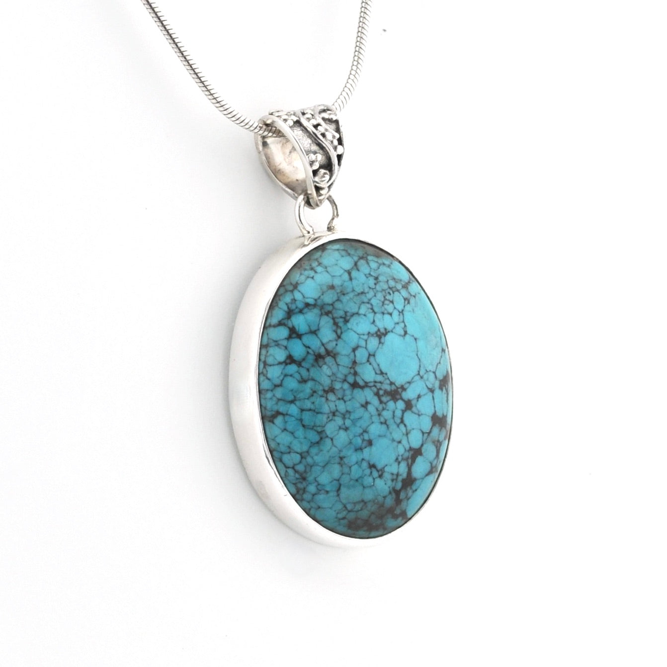 An oval pendant necklace featuring a vibrant turquoise stone with dark matrix veining, set in a polished silver bezel on a silver snake chain.
