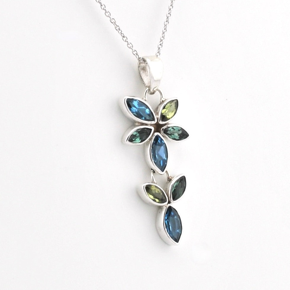 A silver floral pendant necklace featuring marquise-cut blue and olive green stones, displayed on a clean white background.