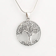 A silver pendant necklace featuring a circular tree of life design with intricate scrollwork, suspended from a fine silver chain against a plain white background.