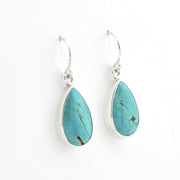 A pair of silver drop earrings featuring teardrop-shaped turquoise stones with natural dark veining, set in polished silver bezels on silver French hook ear wires, shown against a plain white background.