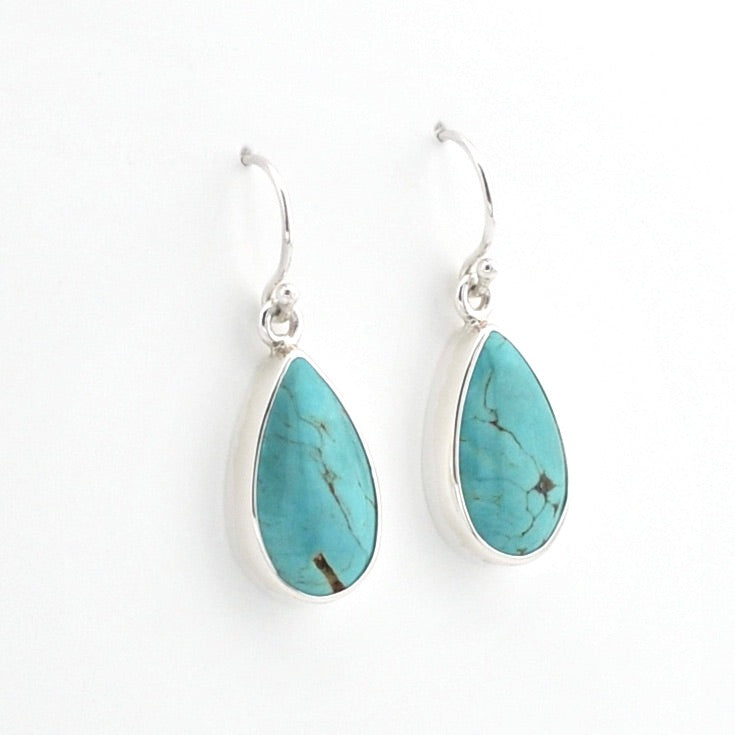 A pair of silver drop earrings featuring teardrop-shaped turquoise stones with natural dark veining, set in polished silver bezels on silver French hook ear wires, shown against a plain white background.