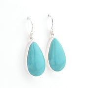 A pair of silver drop earrings featuring teardrop-shaped turquoise gemstones, shown against a plain white background.