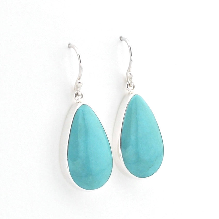 A pair of silver drop earrings featuring teardrop-shaped turquoise gemstones, shown against a plain white background.