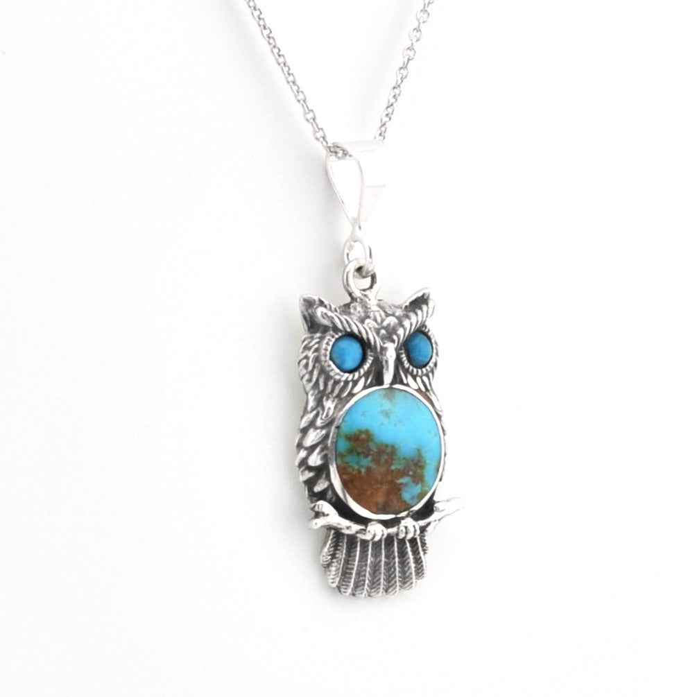 A sterling silver owl pendant necklace featuring a large oval turquoise stone with brown matrix inlay for the body, and two smaller round turquoise stones for the eyes, shown on a white background.